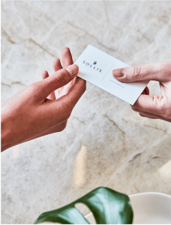 two hands exchanging a sollis health business card over marble background