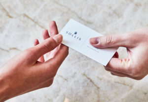 two hands exchanging a sollis health business card over a marble background